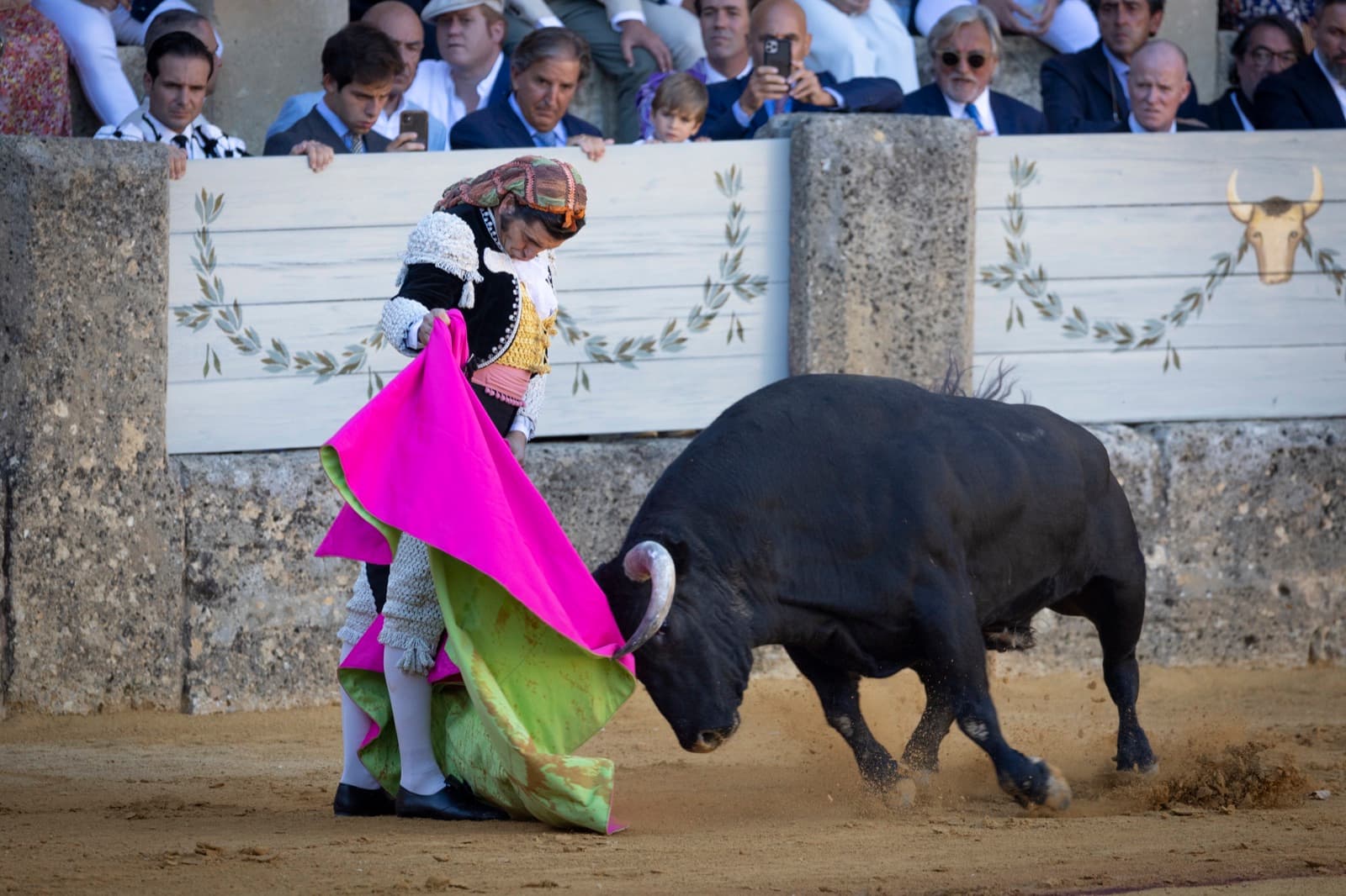 Morante de la Puebla, vestido de goyesco, templa la embestida del toro con el capote junto al burladero en la Goyesca de 2022